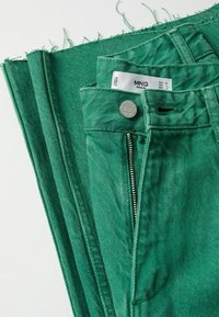 Pantaloni in denim verdi stesi, con zip, chiusura a bottone e orlo sfrangiato. L'etichetta mostra la marca MNG e i dettagli della taglia.