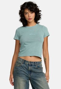 Jasnoniebieski, krótki t-shirt z krótkim rękawem, z małą białą metką RVCA. Noszony z wysokim stanem niebieskich dżinsów.