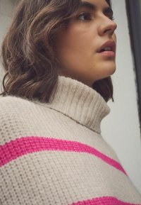 Beige turtleneck sweater med lyserøde striber, der har et struktureret strikmønster, fremhæver et blødt, cozy stof og afslappet pasform.