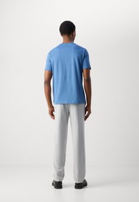 Blauwe katoenen T-shirt met korte mouwen, gecombineerd met lichtgrijze broek. De outfit heeft een relaxte pasvorm en een minimalistisch ontwerp.