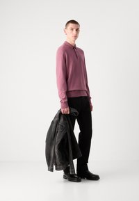 Hosszú ujjú, slim-fit, mályva színű pólóing, texturált anyagból, gallérral és három gombbal, fekete nadrággal és sötét farmerdzsekivel párosítva.