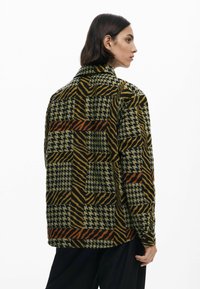 Mønstret patchworkjakke i flere farver med houndstooth og stribede mønstre i mørkegrøn, sort, orange og gul. Tekstureret design med krave.