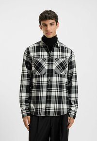 Zwart-wit geruite flanellen shirt met twee borstzakken, knoopsluiting aan de voorkant en lange mouwen. Zachte textuur en relaxte pasvorm.