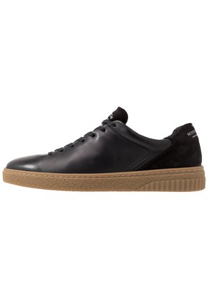 Sort læder lavtop sneaker med sorte snørebånd og tan gummisål, der viser sideprofil på hvid baggrund.