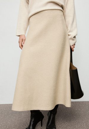Beige wool skirt with a fluid A-line shape, knee-length, featuring a soft texture and minimal seams, paired with a black bag.