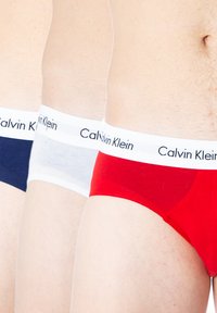 Tre paia di slip Calvin Klein: blu navy, bianco e rosso. Ognuno presenta un elastico bianco con la scritta del marchio in nero. Tessuto dalla consistenza liscia.