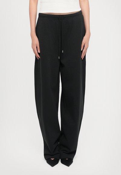 Pantalons de survêtement noirs avec une coupe décontractée, taille élastique et cordon de serrage. Texture douce et coutures latérales soulignant le design à jambes larges.
