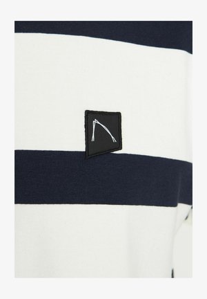 Dryžuota medvilninė marškinėliai su tamsiai mėlynais ir baltais horizontaliais dryžiais, su juodu stačiakampiu etikete, turinčia minimalistinį baltą dizainą.