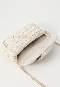 Crochet handbag in cream with a textured pattern, featuring a gold snap closure and chain strap, lined with a soft beige interior.