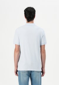 Lys blå kortermet polo skjorte med flat krage. Myk, glatt tekstur og klassisk passform, kombinert med lyse denimjeans.