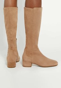 Knee-high beige suede boots with a block heel, featuring a smooth texture and side zipper closure for easy wear.