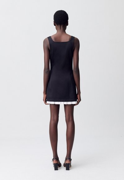 Vestido negro sin mangas con un escote cuadrado, que presenta un dobladillo con un ribete blanco plisado. Tela suave y silueta ajustada.