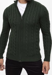 Donkergroene vest met ritssluiting, voorzien van een gestructureerd kabelgebreid patroon, geribbelde manchetten en zoom, met een opstaande kraag en een soepele ritssluiting.