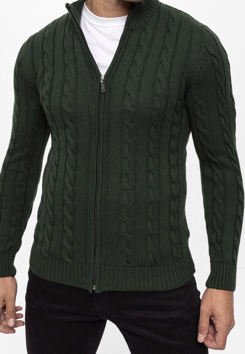 Donkergroene vest met ritssluiting, voorzien van een gestructureerd kabelgebreid patroon, geribbelde manchetten en zoom, met een opstaande kraag en een soepele ritssluiting.