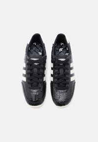 Black sneakers with a textured snake-print upper, white leather stripes, and black laces. White sole with logo print on the insole.