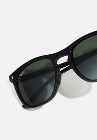 Black plastic sunglasses with dark green lenses, featuring a distinct geometric shape, wide frames, and Ray-Ban logo on the side.