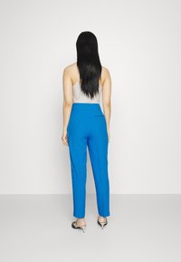 Pantaloni blu su misura realizzati in tessuto liscio, con una vestibilità slim e dettagli delle tasche posteriori, abbinati a una canotta leggera e tacchi neri.