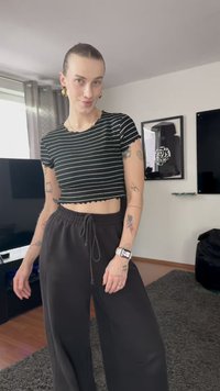 Top scurt cu dungi alb-negru, cu tiv ondulat, asortat cu pantaloni largi din bumbac negri. Accesoriile includ cercei mari din aur și o adresă.