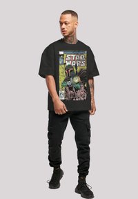 Svart oversized t-skjorte med et fargerikt tegneserieinspirert illustrasjon av Boba Fett fra Star Wars foran. Materialene er ikke spesifisert.