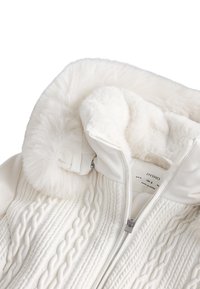 Giacca imbottita bianca con collo in pelliccia sintetica, caratterizzata da un design a trecce lavorate a maglia, chiusura con cerniera e fodera interna morbida.