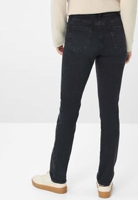 Jeans neri aderenti con una texture liscia, design a cinque tasche e dettagli di cucitura sottili. Indossati con sneakers di colore chiaro.