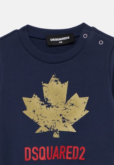 Navy blå bomullsbody med en slitt gull lønnbladgrafikk og rød "DSQUARED2"-tekst. Har trykknapper på skulderen.
