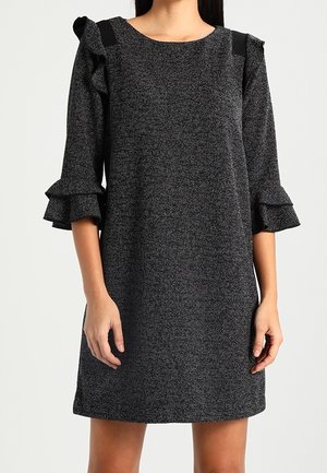 Mørkegrå tekstureret knælængde kjole med flæsekanter på 3/4 ærmer og sorte skulderdetaljer på en stående person.