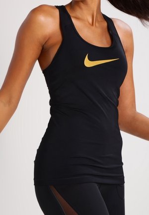 Kvinde iført sort atletisk tanktop med gul Nike-logo og sorte leggings med meshpaneler på siderne.