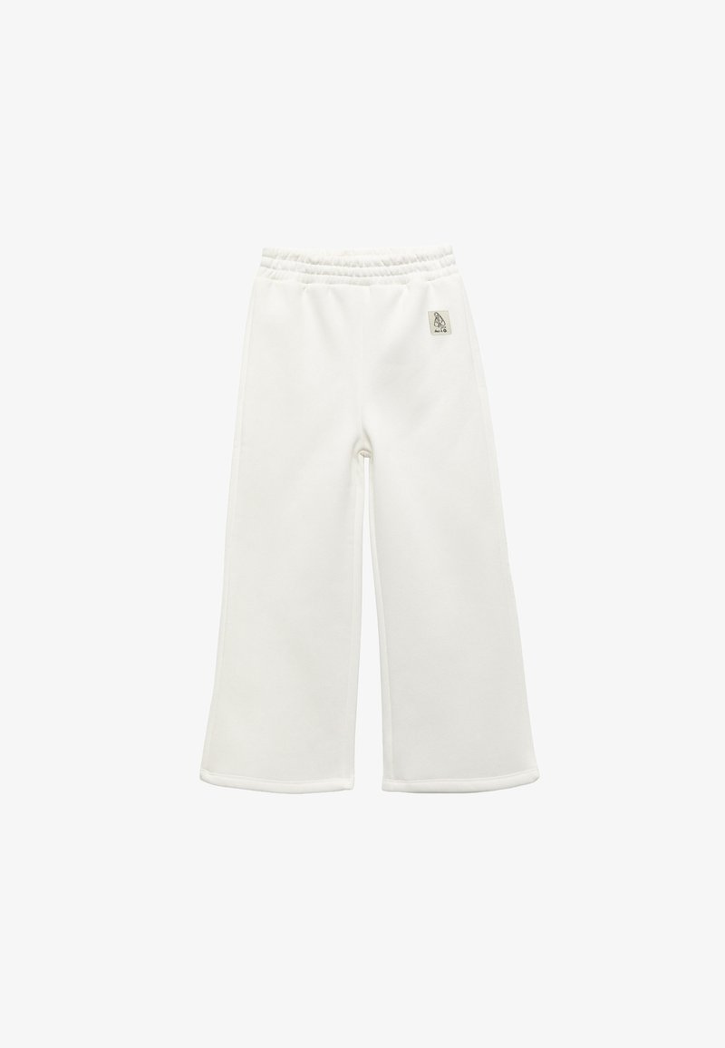 Pantalones amplios blancos con cinturilla elástica y un pequeño parche de logo en la cadera derecha, dispuestos sobre un fondo blanco.