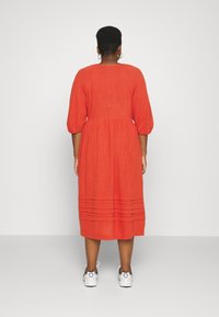Robe midi en lin rouge avec des manches bouffantes et un ourlet plissé en tierces, stylée avec des baskets blanches, vue de dos.