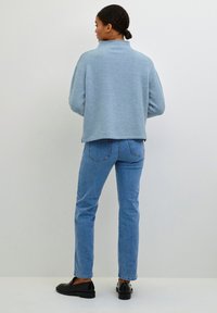 Maglione a maniche lunghe di un azzurro chiaro, dal texture soffice, con colletto alto, abbinato a jeans dritti azzurri chiari e scarpe nere.