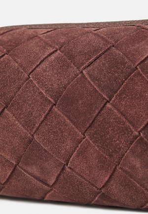 Nærbillede af et vævet mørkebrunt ruskindsmateriale, der danner et tekstureret lapværksmønster med synligt søm.