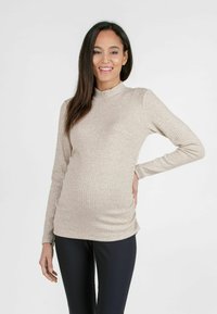 Beige geripptes Langarmshirt mit hohem Kragen und seitlichen Raffungen, kombiniert mit schwarzen, figurbetonten Hosen. Weicher Stoff und schlank geschnittenes Design.