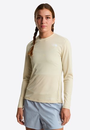 Długi rękaw, jasnobeżowa sportowa koszulka z teksturowanym wzorem kratki, z subtelnym logo na piersi. Gładkie wykończenie tkaniny.