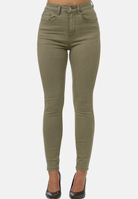 Vaqueros ajustados de cintura alta en tejido de algodón elástico color caqui, con cinco bolsillos y un acabado suave. Combinados con tacones negros.