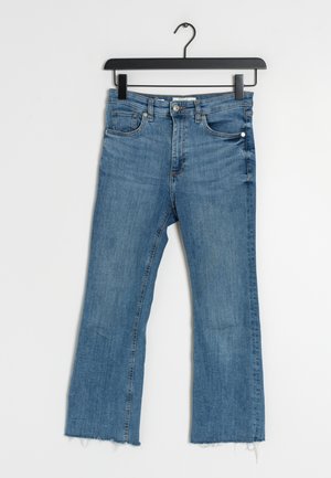 Jean flare en denim bleu clair suspendu sur un cintre noir, comportant cinq poches, un ourlet effiloché et des coutures contrastées.