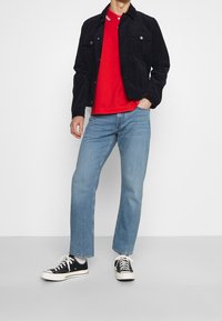 Chaqueta de pana navy sobre una camiseta polo roja, combinada con jeans rectos de color azul claro y zapatillas de lona negras con suelas blancas.