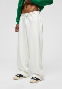 Witte sweatpants met een elastische tailleband, een trekkoord en zijzakken, gecombineerd met zwarte schoenen met witte veters en een gestructureerde zool.