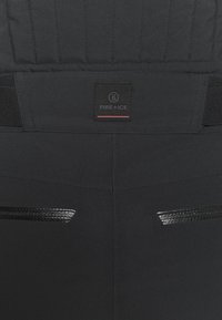 Mustat urheiluhousut, joissa tikattu vyötärö, merkkilappu ja kiiltävät, tyylikkäät yksityiskohdat kahdessa takataskussa.