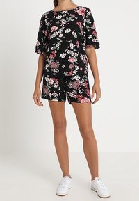 Conjunto floral que incluye una parte superior negra y pantalones cortos a juego, con patrones de flores en rosa y blanco. Diseñado con mangas cortas y un ajuste relajado.