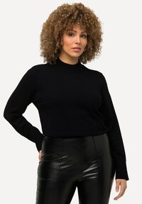 Schwarzer Strickpullover mit hohem Kragen und langen Ärmeln, kombiniert mit eng anliegenden schwarzen Kunstlederhosen. Glatte Textur und minimalistisches Design.