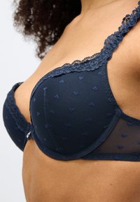 Σουτιέν ναυτικού μπλε χρώματος από δίχτυ και δαντέλα, με μικρά μοτίβα καρδιάς, διακοσμητική δαντέλα στα άκρα και ρυθμιζόμενους ιμάντες.