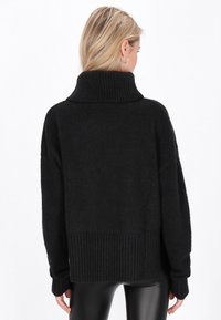 Pulover negru, supradimensionat, cu guler înalt, tiv și manșete în dungi; textură moale, cu umeri căzuți și croială lejeră.