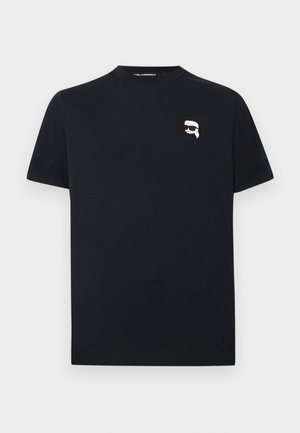 T-shirt noir à manches courtes avec un petit visage de dessin animé blanc portant des lunettes de soleil noires sur le côté gauche de la poitrine.