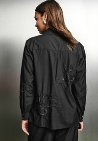 Mustam puuvillane särk pikkade varrukatega. Seljal on keeruline must embroideria lillemotiivides. Nööbitavad varrukasuud ja krae.