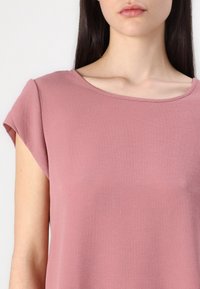 Top a maniche corte in morbido tessuto rosa con una texture liscia e scollatura rotonda, caratterizzato da una vestibilità comoda e dettagli di cucitura minimi.