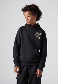 Μαύρο φούτερ με μαλακό ύφασμα, διαθέτει μπροστινή τσέπη και χρυσό λογότυπο Levi's με γραφικό σχέδιο αλόγου στο στήθος.