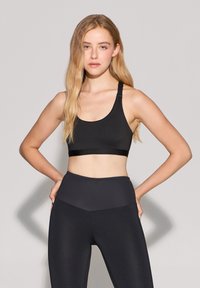 Top sportivo nero con texture liscia, spalline larghe e fascia di supporto. Abbinato a leggings neri a vita alta con design senza cuciture.
