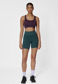 Bordeauxroze sportbeha en donkergroene high-waisted shorts, beide gemaakt van glad materiaal. Voorzien van een geribbelde textuur en een aansluitend ontwerp.