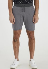 Pantalones cortos deportivos grises con cintura ajustable, que presentan una textura suave y un dobladillo ligeramente deshilachado, combinados con zapatillas blancas.